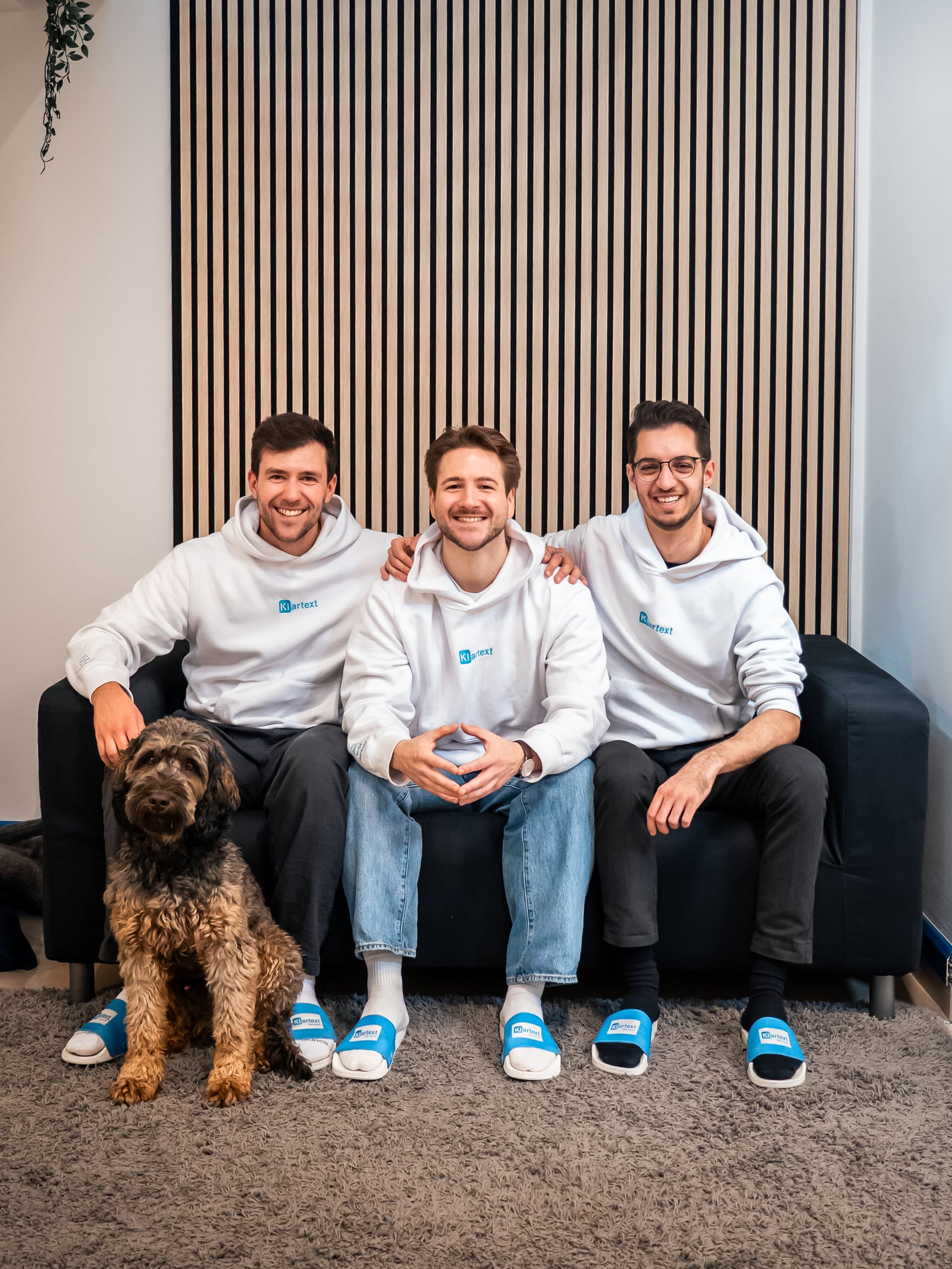The three Klartext AI founders with office dog Bruno on the sofa. From left: Daniel Toth, Ruben Hetfleisch, Felix Krause.