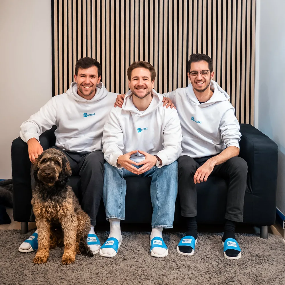 The three Klartext AI founders with office dog Bruno on the sofa. From left: Daniel Toth, Ruben Hetfleisch, Felix Krause.